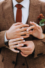 A stylish groom in a brown suit with a boutonniere and the bride put gold rings on their fingers. Wedding photography, portrait.