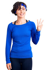 Obraz na płótnie Canvas Beautiful young woman with short hair wearing training workout clothes showing and pointing up with fingers number three while smiling confident and happy.