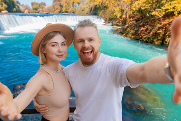 Fototapeta premium Happy tourist woman and man make selfie photo on smartphone background waterfall summer Manavgat Antalya. Concept travel trip Turkey