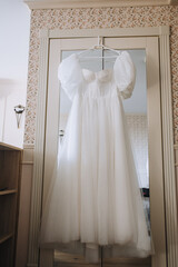 A beautiful white long wedding dress hangs on a hanger in a closet with a mirror.
