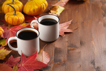 Two white cups with black coffee in a cozy autumn setting with red, yellow and orange leaves, hokkaido pumpkins, on wooden background