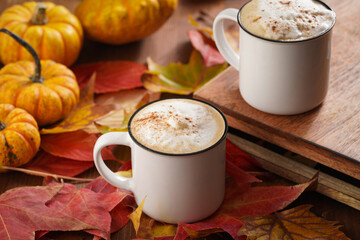 Obraz na płótnie Canvas Two white cups with black coffee and white milk foam and cinnamon spice in a cozy autumn setting with red, yellow and orange leaves, hokkaido pumpkins, on wooden background