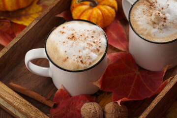 Two white cups with black coffee and white milk foam and cinnamon spice in a cozy autumn setting with red, yellow and orange leaves, hokkaido pumpkins, on wooden background