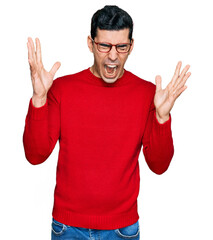 Naklejka premium Handsome hispanic man wearing casual clothes and glasses celebrating mad and crazy for success with arms raised and closed eyes screaming excited. winner concept