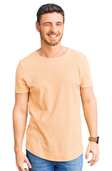 Fototapeta premium Handsome young man with bear wearing casual yellow tshirt winking looking at the camera with sexy expression, cheerful and happy face.