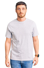 Fototapeta premium Handsome young man with bear wearing casual tshirt puffing cheeks with funny face. mouth inflated with air, crazy expression.