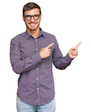Handsome caucasian man wearing casual clothes and glasses smiling and looking at the camera pointing with two hands and fingers to the side.