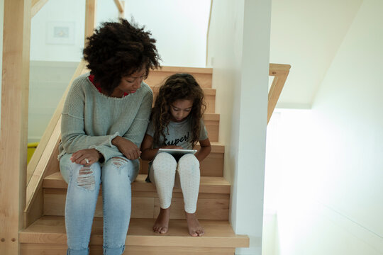 Mother and daughter using digital tablet on wooden stairs