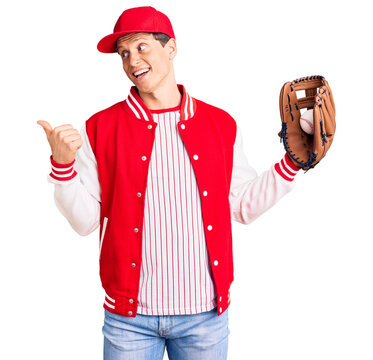 Young handsome man wearing baseball uniform holding golve and ball pointing thumb up to the side smiling happy with open mouth