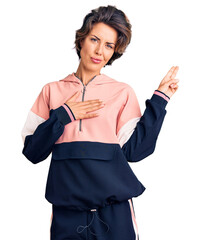 Young beautiful woman wearing sportswear smiling swearing with hand on chest and fingers up, making...