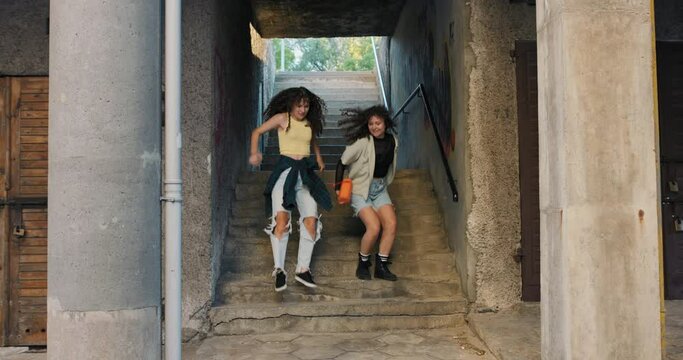 Happy, contented teenagers carelessly run down the stairs on the estate holding a portable speaker with music on. Surrounded by graffiti the austere environment.