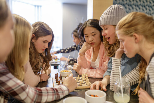 Tween girl friends playing chess, hanging out at cafe table