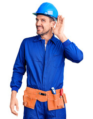 Young handsome man wearing worker uniform and hardhat smiling with hand over ear listening an hearing to rumor or gossip. deafness concept.