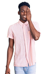 Young african american man wearing casual clothes covering one eye with hand, confident smile on face and surprise emotion.