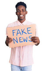 Young african american man holding fake news banner looking positive and happy standing and smiling...