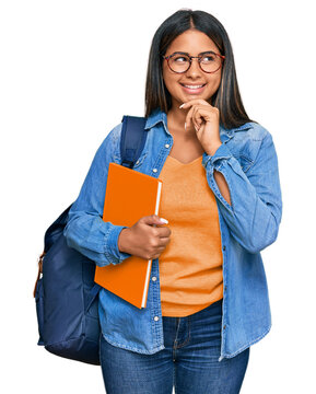 Young latin girl wearing student backpack and holding books with hand on chin thinking about question, pensive expression. smiling and thoughtful face. doubt concept.