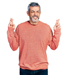 Middle age hispanic with grey hair wearing casual sweater gesturing finger crossed smiling with hope and eyes closed. luck and superstitious concept.