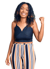 Young african american woman wearing casual clothes smiling with happy face looking and pointing to the side with thumb up.