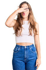 Fototapeta premium Beautiful caucasian young woman wearing casual clothes and glasses peeking in shock covering face and eyes with hand, looking through fingers with embarrassed expression.