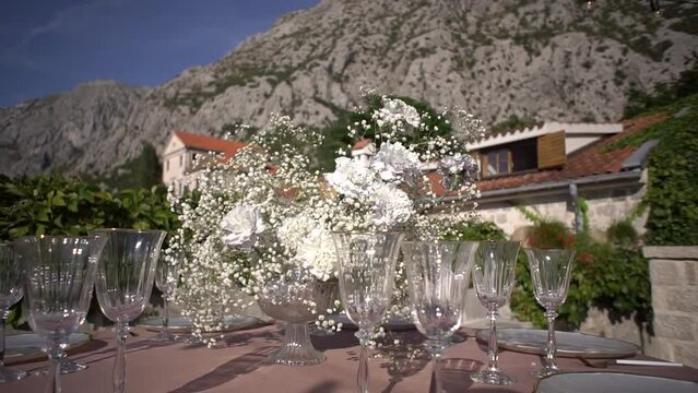 Vase with white flowers surrounded by glasses on a table in the courtyard of the building