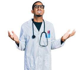 Fototapeta premium Young african american man wearing doctor uniform and stethoscope crazy and mad shouting and yelling with aggressive expression and arms raised. frustration concept.