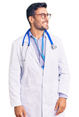 Young hispanic man wearing doctor uniform and stethoscope looking away to side with smile on face, natural expression. laughing confident.