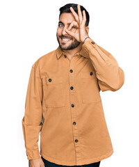 Young hispanic man wearing casual clothes doing ok gesture with hand smiling, eye looking through fingers with happy face.