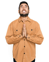 Young hispanic man wearing casual clothes begging and praying with hands together with hope expression on face very emotional and worried. begging.
