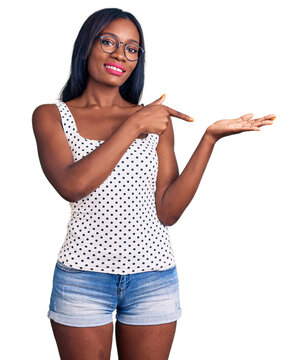Young african american woman wearing casual clothes and glasses amazed and smiling to the camera while presenting with hand and pointing with finger.
