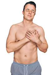 Fototapeta premium Handsome young man wearing swimwear shirtless smiling with hands on chest with closed eyes and grateful gesture on face. health concept.