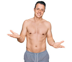 Fototapeta premium Handsome young man wearing swimwear shirtless smiling cheerful with open arms as friendly welcome, positive and confident greetings