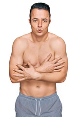 Fototapeta premium Handsome young man wearing swimwear shirtless shaking and freezing for winter cold with sad and shock expression on face