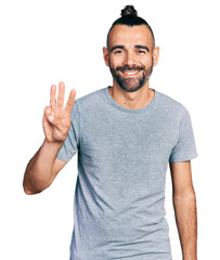 Naklejka premium Hispanic man with ponytail wearing casual grey t shirt showing and pointing up with fingers number three while smiling confident and happy.