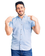 Young hispanic man wearing casual clothes looking confident with smile on face, pointing oneself with fingers proud and happy.