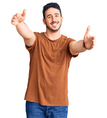 Naklejka premium Young hispanic man wearing casual clothes looking at the camera smiling with open arms for hug. cheerful expression embracing happiness.