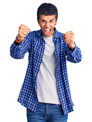 Young african amercian man wearing casual clothes angry and mad raising fists frustrated and furious while shouting with anger. rage and aggressive concept.