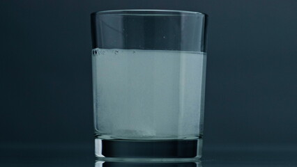 Fizzy medicine water glass at dark background closeup. Acid air bubbles rising