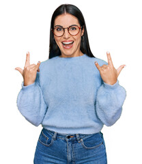 Young hispanic woman wearing casual clothes and glasses shouting with crazy expression doing rock symbol with hands up. music star. heavy concept.