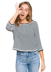 Beautiful blonde woman wearing casual clothes doing ok gesture shocked with surprised face, eye looking through fingers. unbelieving expression.