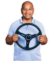 Hispanic middle age man holding steering wheel smiling with a happy and cool smile on face. showing teeth.