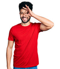 Young arab man with beard wearing casual red t shirt doing ok gesture with hand smiling, eye looking through fingers with happy face.