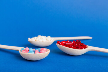Vitamin capsules in a spoon on a colored background. Pills served as a healthy meal. Red soft gel vitamin supplement capsules on spoon