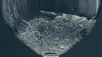Closeup water pouring glass at dark background. Splashing fluid filling cup