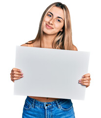 Fototapeta premium Hispanic young woman holding blank empty banner relaxed with serious expression on face. simple and natural looking at the camera.