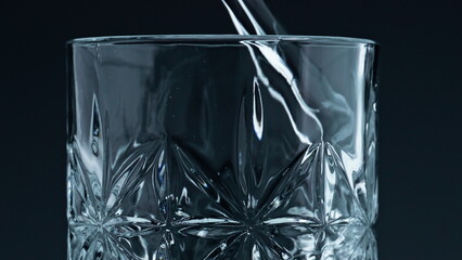 Closeup water pouring glass with splashing dark background. Crystal fresh liquid