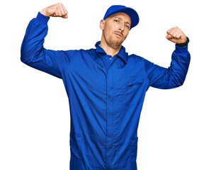 Bald man with beard wearing builder jumpsuit uniform showing arms muscles smiling proud. fitness concept.