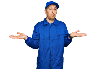 Bald man with beard wearing builder jumpsuit uniform clueless and confused expression with arms and hands raised. doubt concept.