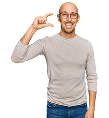 Bald man with beard wearing casual clothes and glasses smiling and confident gesturing with hand doing small size sign with fingers looking and the camera. measure concept.