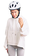 Beautiful brunette young woman wearing bike helmet and sporty clothes angry and mad raising fist frustrated and furious while shouting with anger. rage and aggressive concept.
