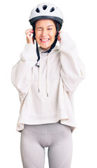 Beautiful brunette young woman wearing bike helmet and sporty clothes covering ears with fingers with annoyed expression for the noise of loud music. deaf concept.